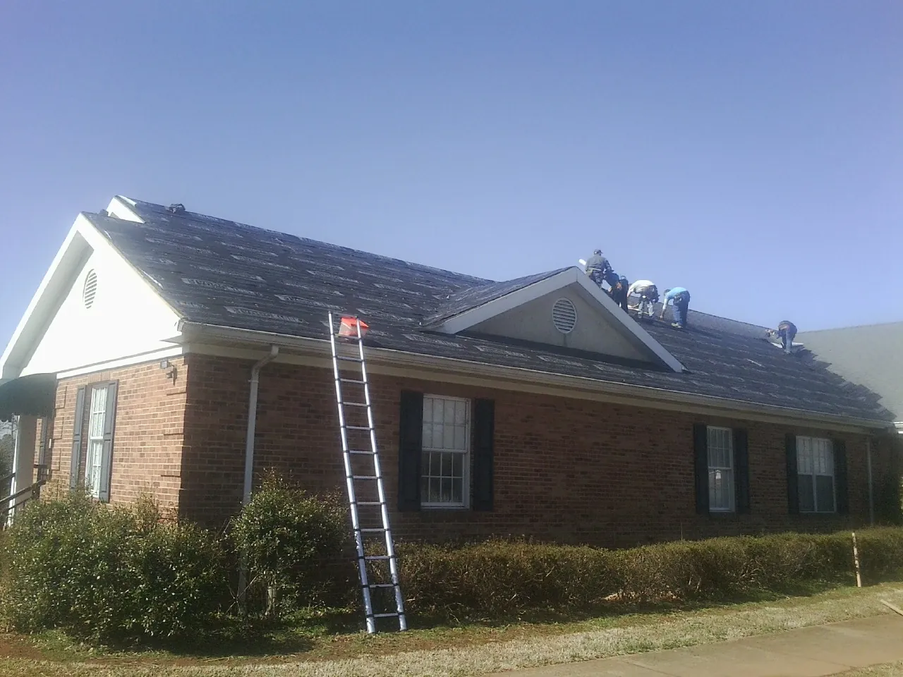 Crew tearing shingles off a brick ranch roof with a ladder set — Emergency Roof Repair work by our crew in Lutherville Timonium
