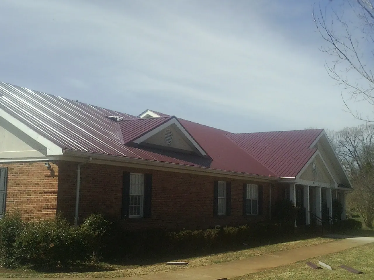 Red metal roof with gabled entries on a long brick building, from a Hail Damage Roof Repair job in Lutherville Timonium