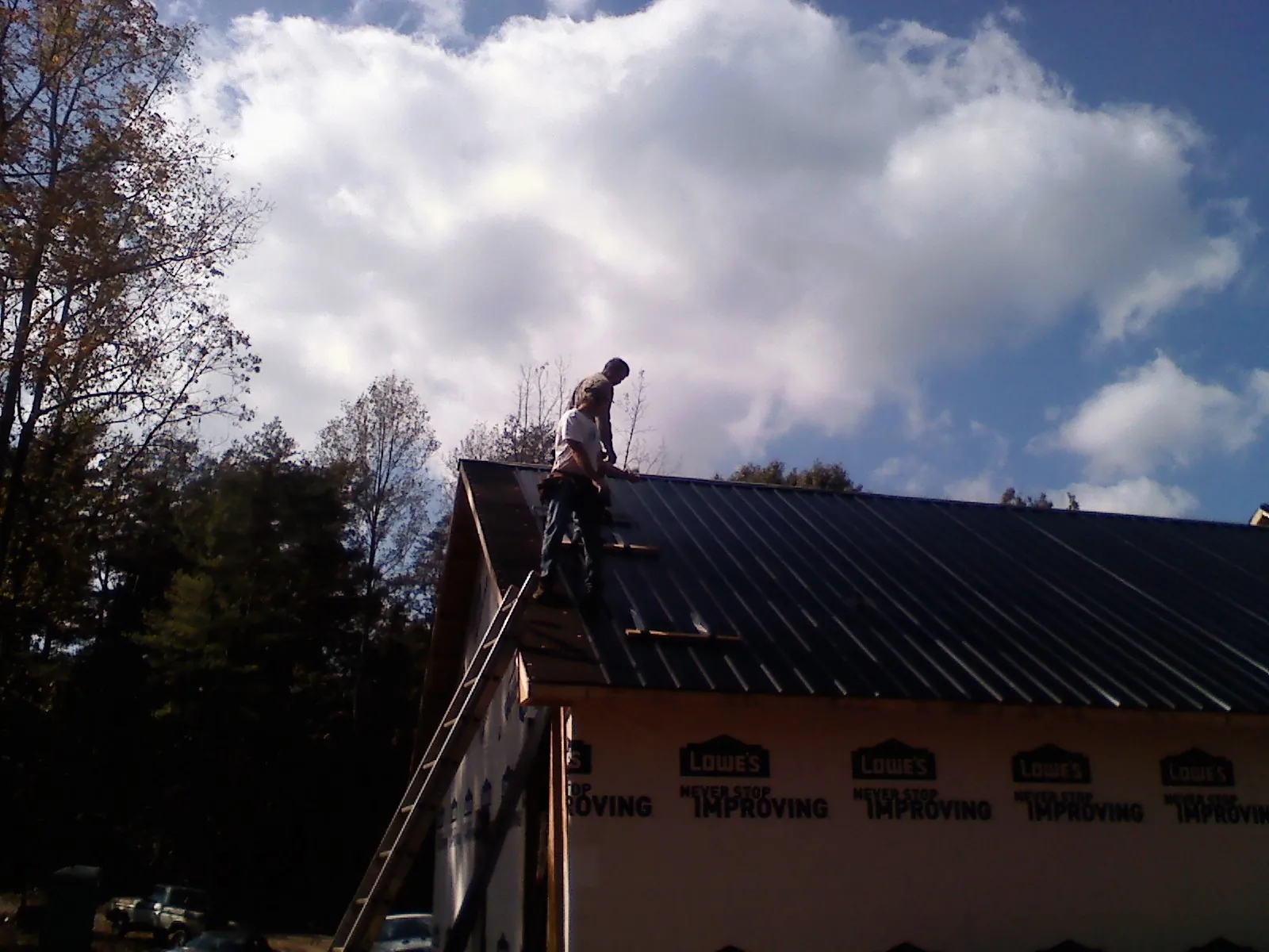 Roofer fastening dark metal panels high against a cloudy sky, from a Roof Inspection job in Lutherville Timonium