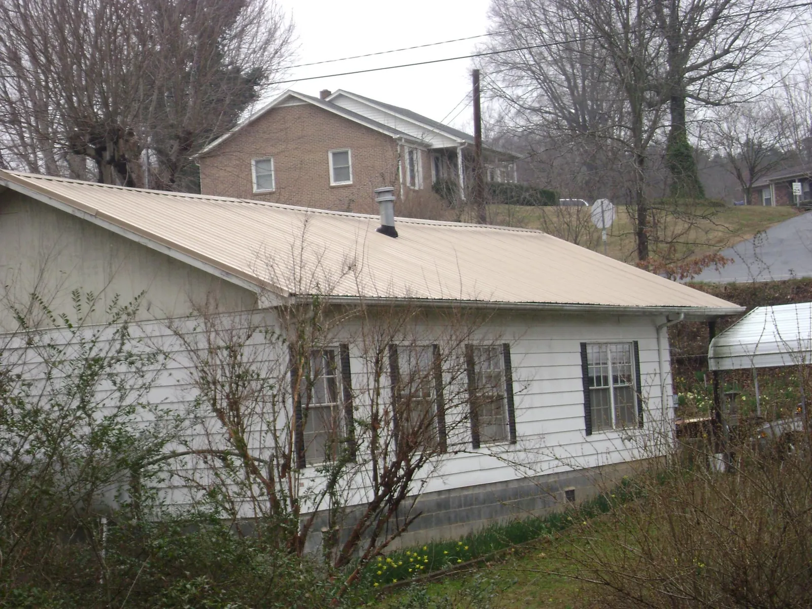 Tan metal roof on a white sided house set into a hillside — Commercial Roofing by Roofing Brothers in Lutherville Timonium